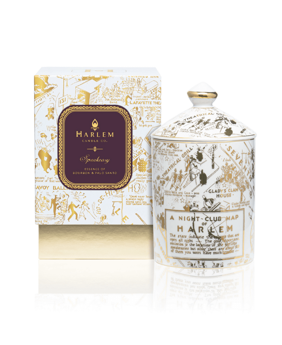 Our Speakeasy Map Ceramic Candle with Lid with the Night Club Map of Harlem etched in gold on the ceramic with a white background sitting next to its decorative box.