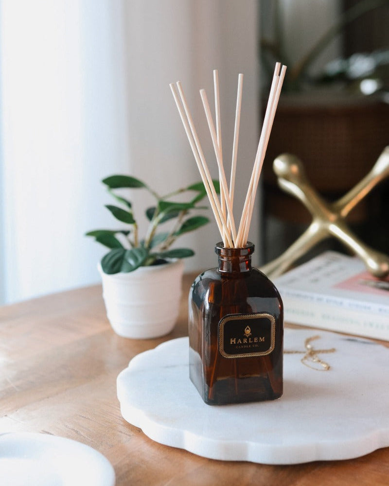 Our 8 fluid oz. Savoy Reed Diffuser with reeds, in a brown glass vessel sitting on a wooden table.