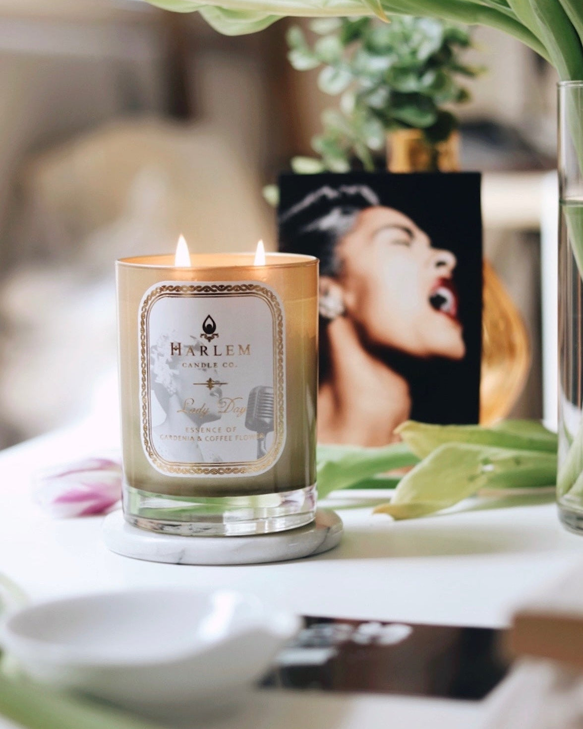 Lifestyle image of our Lady Day candle with green leaves in the background.
